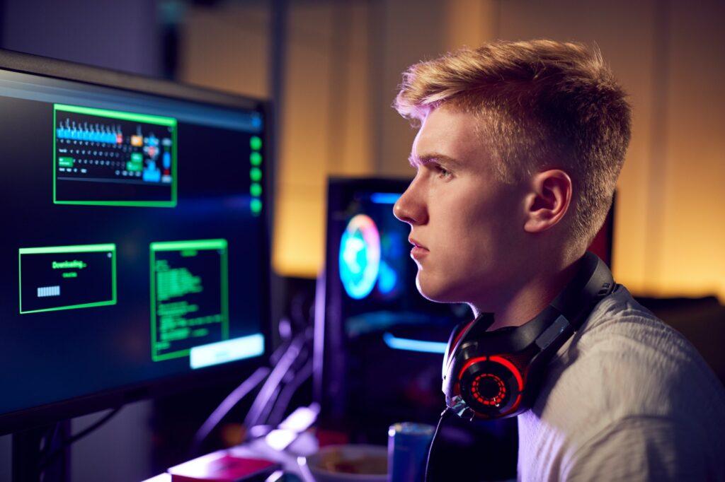 male teenage hacker sitting in front of computer screens bypassing cyber security